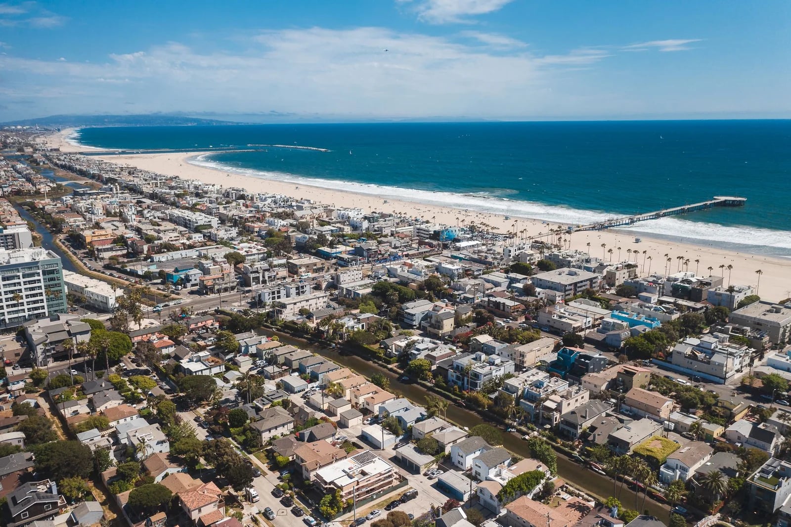 A stunning aerial view of a coastal urban city with a vibrant beach and pier.